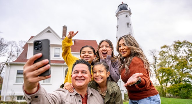 family taking selfie with milwaukee's north point lighthouse in the background