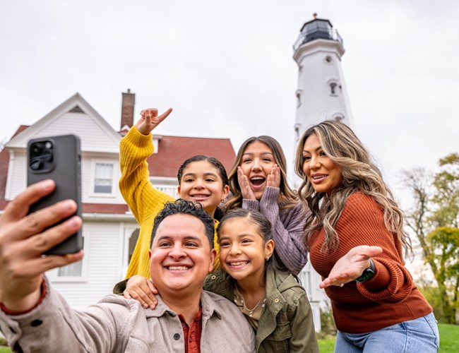 family taking selfie with milwaukee's north point lighthouse in the background
