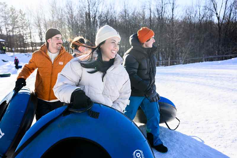friends walking up a snow hill carrying snow tubes
