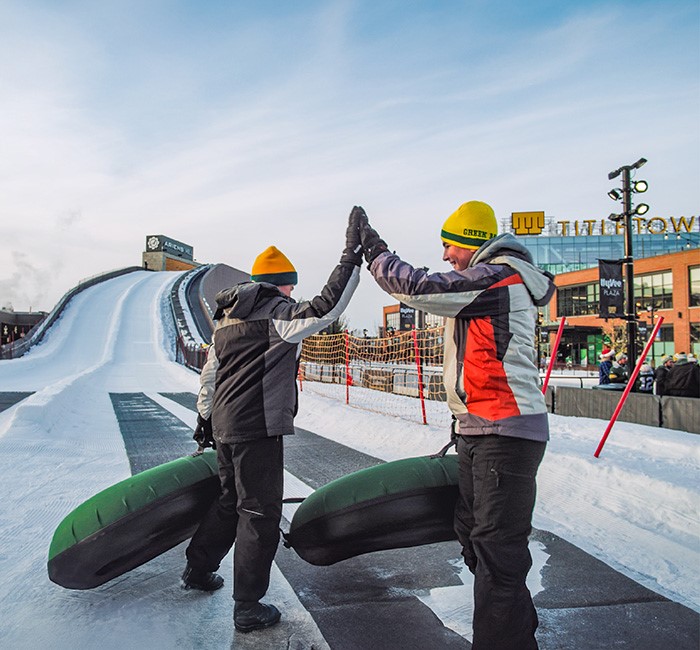 Two people high five at the bottom of a snow tube slide